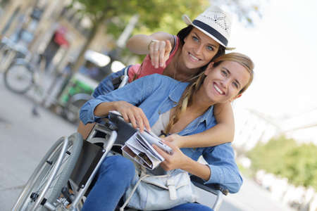 two friends visiting foreign city one sitting in wheelchairの写真素材