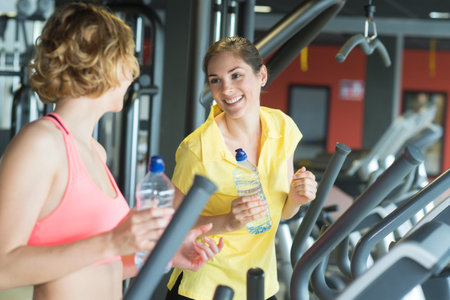 two happy women with bottles of water talking in gym