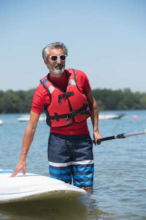man next to a stand-up paddle board on the lakeの写真素材