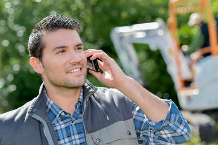 Man outdoors on telephone, digger in backgroundの写真素材