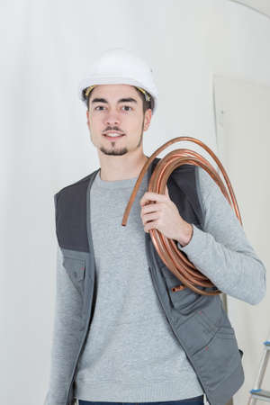Portrait of man holding roll of copper pipeの写真素材