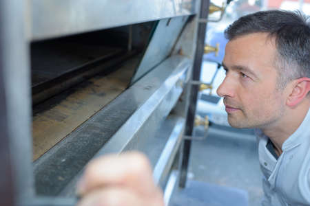 Baker looking in bread ovenの写真素材