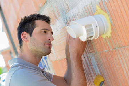 Man fixing vent to exterior wallの写真素材