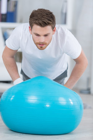 attractive young man with swiss ball doing exercises at homeの写真素材