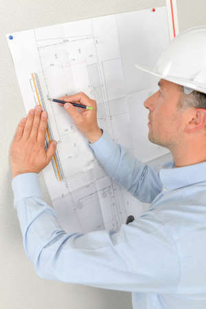 Man measuring plans pinned to wallの写真素材