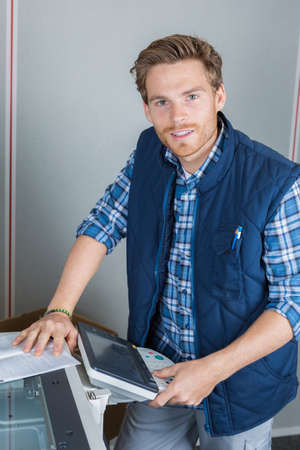 young male technician is repairing a printer at officeの写真素材