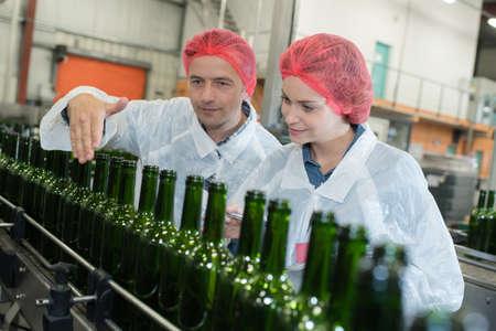 People overseeing wine bottles go down production lineの写真素材