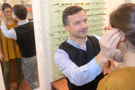 ophthalmologist and beautiful brunette female choosing glasses in optics storeの写真素材