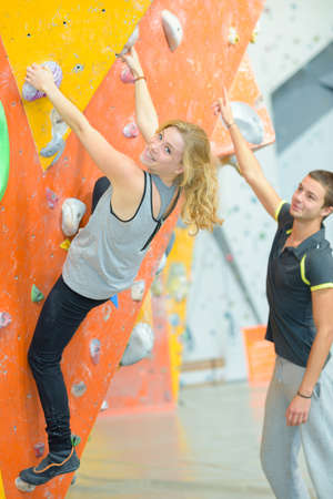 instructor guiding woman on rock climbing wall at the gymの写真素材