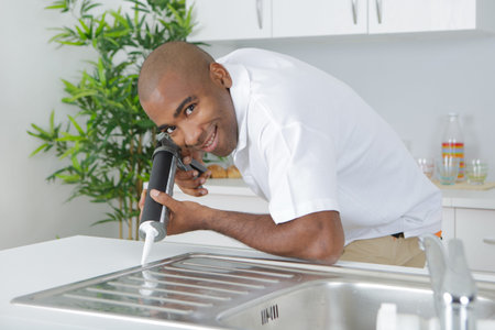 Man sealing edge of kitchen sinkの写真素材