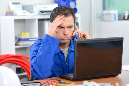 Frustrated man on telephone, looking at computerの写真素材
