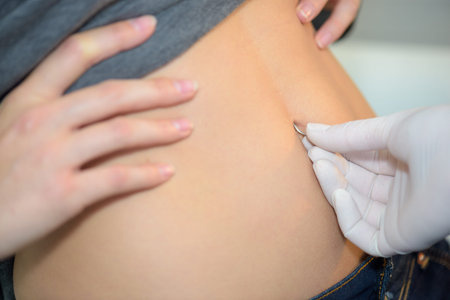 Gloved hand holding piercing to belly buttonの写真素材