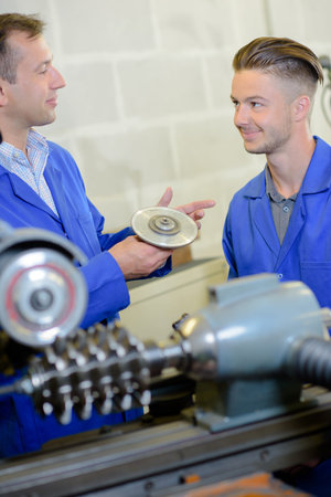 Man showing grinding disk to younger worker