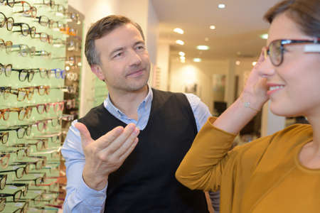 ophthalmologist and beautiful brunette female choosing glasses in optics storeの写真素材