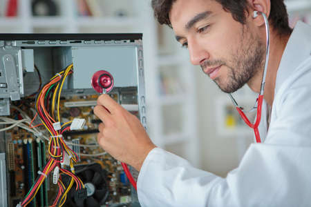 Man holding stethoscope to dismantled computerの写真素材
