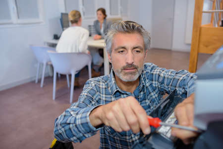 Man repairing office equipment, meeting in backgroundの写真素材
