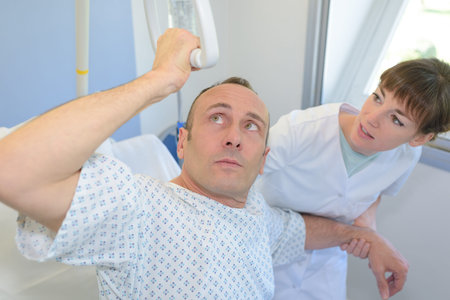 Patient lifting himself out of bed with hoist, nurse helping