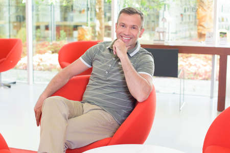 Middle aged man sat in red chairの写真素材