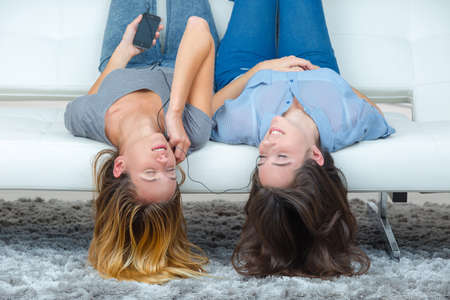 Teenagers upside down on sofa, listening to musicの写真素材