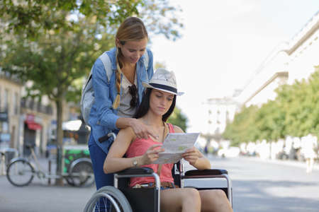 two friends visiting foreign city one sitting in wheelchairの写真素材