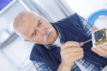 electrician is fixing an outlet with a screwdriverの写真素材