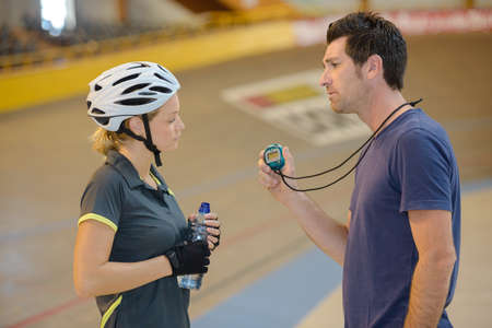 Unsatisfied coach showing stopwatch to cyclistの写真素材
