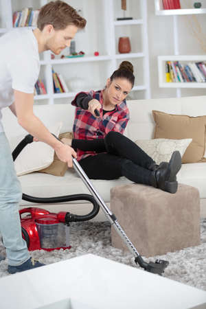 Lady leaning past man vacuuming to change tv channelの写真素材