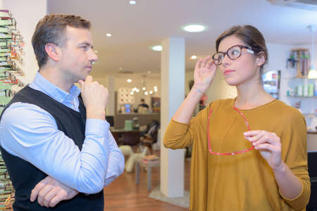 pretty female try eyeglasses with opticianの写真素材