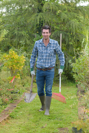 Gardener carrying spade and rake