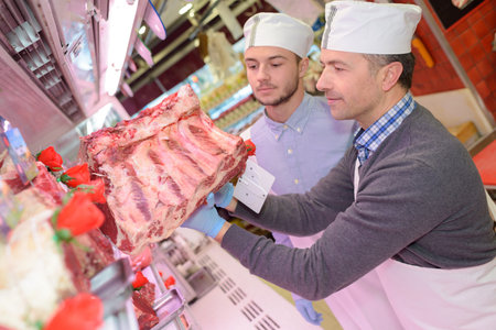 butcher teaching a young one how to sell meat