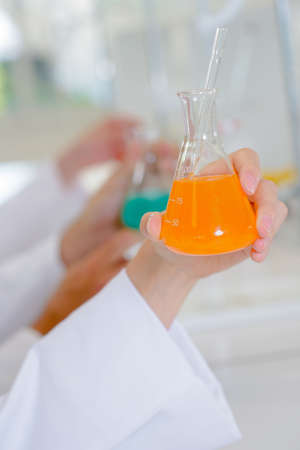 Female hand holding flask containing orange liquidの写真素材