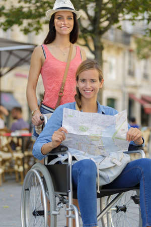 two friends visiting foreign city one sitting in wheelchairの写真素材