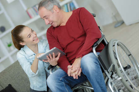 Young lady showing tablet screen to man in wheelchairの写真素材