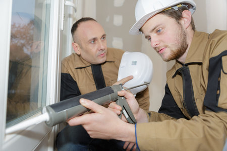 construction worker caulking window with silicone glue using cartridge