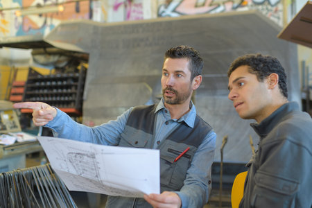 male supervisor with worker discussing over blueprints in industry
