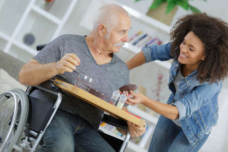 female assistant with senior man in wheelchair at homeの写真素材