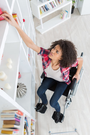 girl in wheelchair reaching for a bookの写真素材
