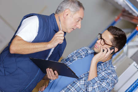 man and co-woker with clipboard and smartphone at warehouseの写真素材