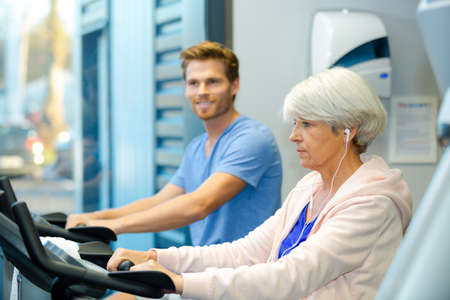 young man and elderly lady using exercise machinesの写真素材