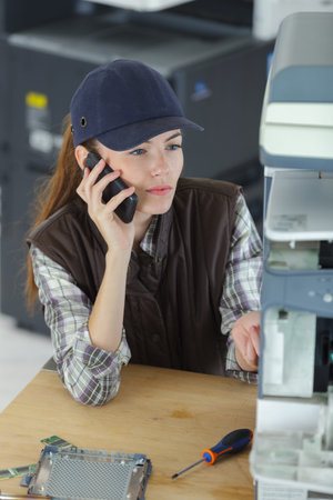 Technician repairing photocopier and talking on cellphone