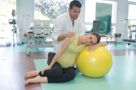 Doctor helping pregnant lady to relax on to aerobic ball