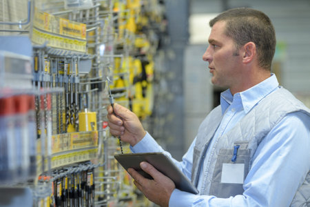 Man with clipboard checking drill bits in store