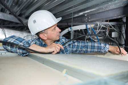 Electrician installing cables into confined spaceの写真素材