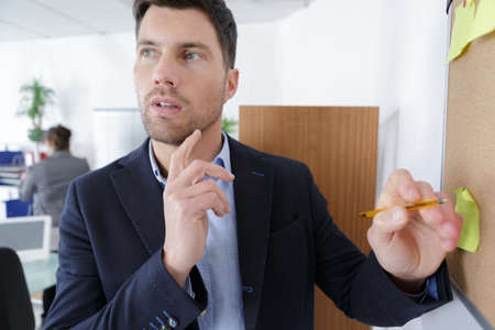 man looking at sticky notes on board in the officeの写真素材