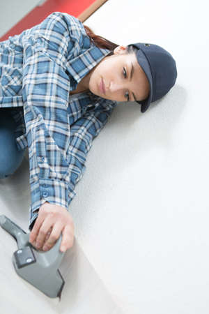 Woman knocking underlay against wall with toolの写真素材