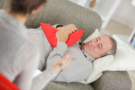 Man clenching cushion while talking to therapistの写真素材