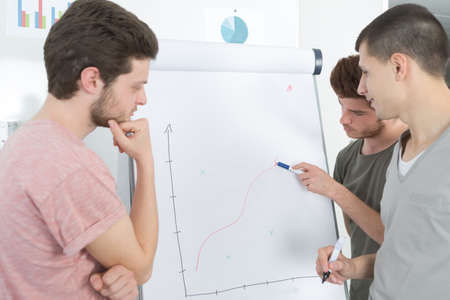 Young men tracing graph on flip chartの写真素材