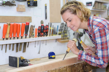 female woodworker with power drill drilling into wood boardの写真素材