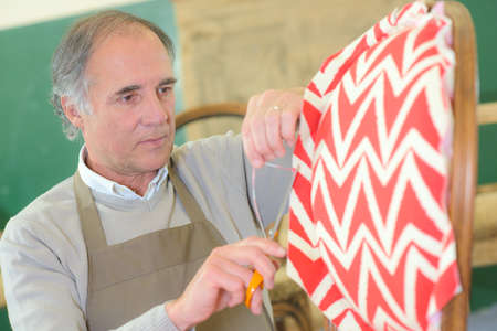 senior man upholstering chair in his workshopの写真素材