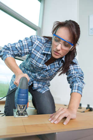 handywoman cutting wooden floor with jigsawの写真素材